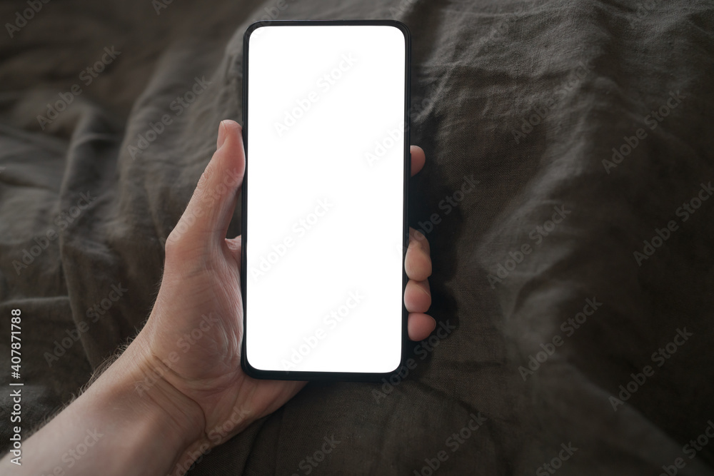 man hand holding phone with white screen over bed on background man hand holding phone with white screen over bed on background