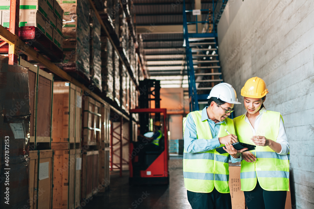 Working at warehouse. asian woman warehouse worker and Manager Shows Digital Tablet Information to further placement in storage department. In Background Stock of Parcels with Products