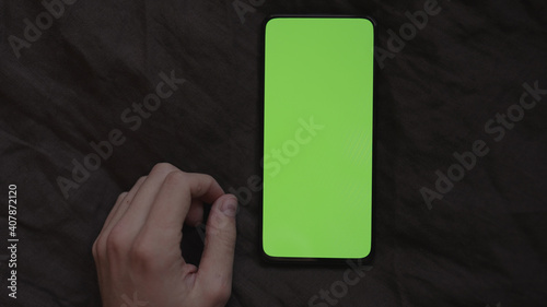 POV man using phone with green screen on linen bed cover