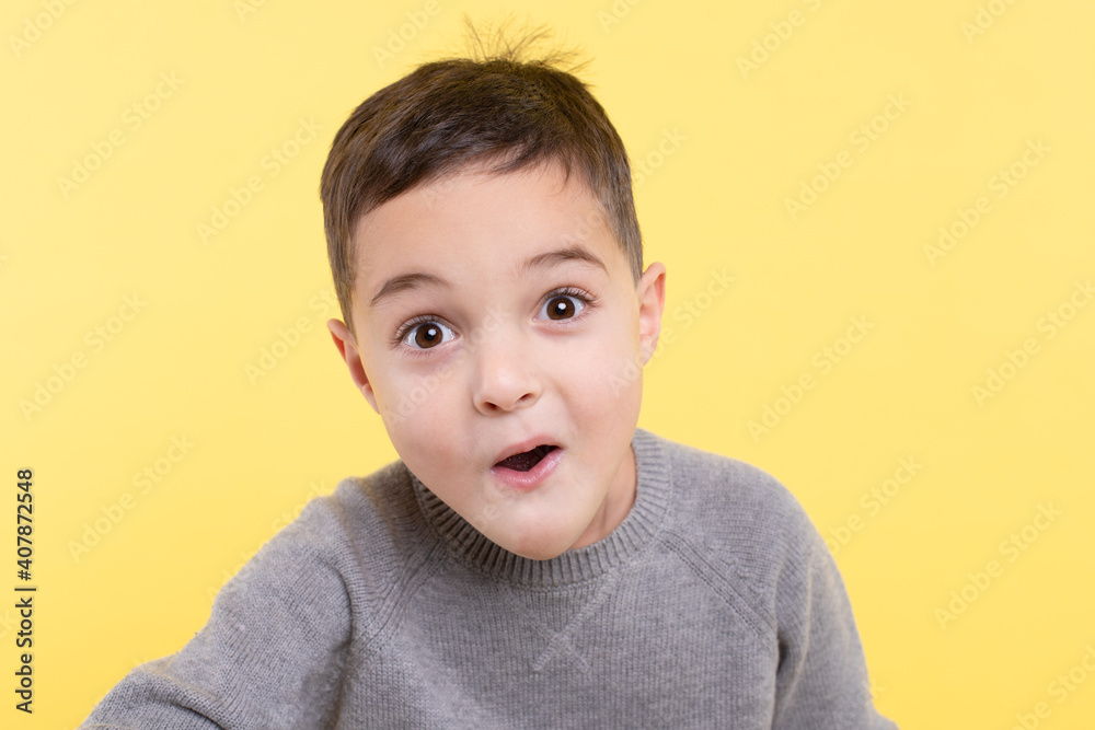 Excited, surprised child on yellow studio background. Primary schoolboy looking at the camera, eye contact, funny open mouth. Positive emotions, shocked face. Close up portrait. Copy space Excited, surprised child on yellow studio background. Primary schoolboy looking at the camera, eye contact, funny open mouth. Positive emotions, shocked face. Close up portrait. Copy space