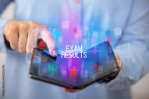 Young man holding a foldable smartphone with EXAM RESULTS inscription, educational concept