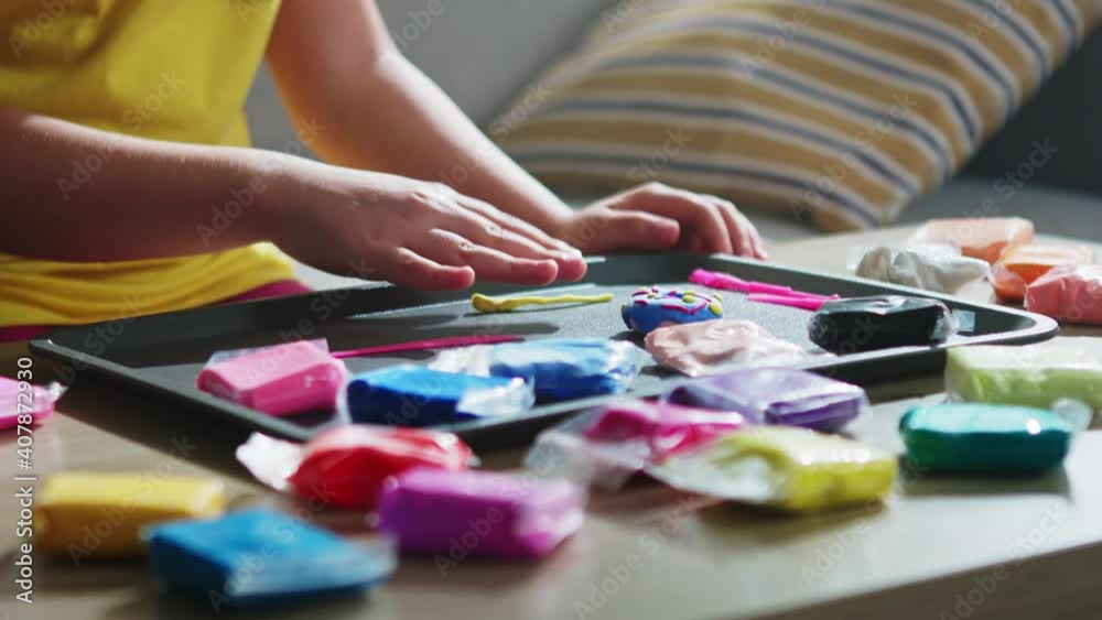 Skillful child is sitting on sofa in living room, sculpting from colorful plasticine, rolling piece of yellow plasticine with her hands, Close up, Slow motion. Skillful child is sitting on sofa in living room, sculpting from colorful plasticine, rolling piece of yellow plasticine with her hands, Close up, Slow motion.