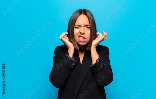 hispanic woman looking angry, stressed and annoyed, covering both ears to a deafening noise, sound or loud music photo