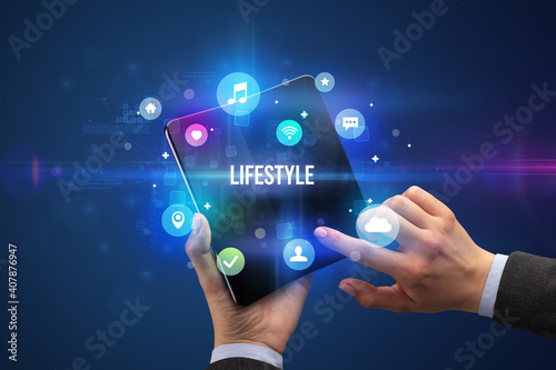 Businessman holding a foldable smartphone with LIFESTYLE inscription, social media concept