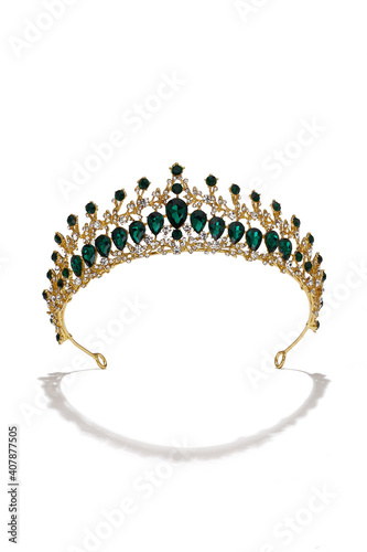 Subject shot of golden tiara adorned with emerald gems and clear sparkling rhinestones that form fanciful pattern. The luxury queen crown is isolated on the white backdrop.