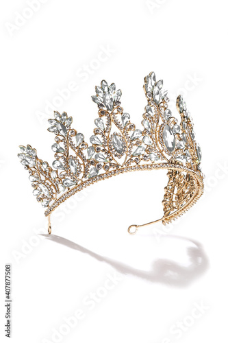 Subject shot of golden tiara adorned with a plenty of diamond-like gems and clear sparkling rhinestones that form fanciful pattern. The luxury queen crown is isolated on the white backdrop.