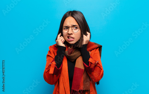 hispanic woman looking angry, stressed and annoyed, covering both ears to a deafening noise, sound or loud music photo