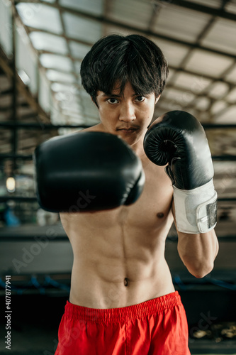 Portrait of professional male boxer make a hitting motion against boxing training ground background © Odua Images