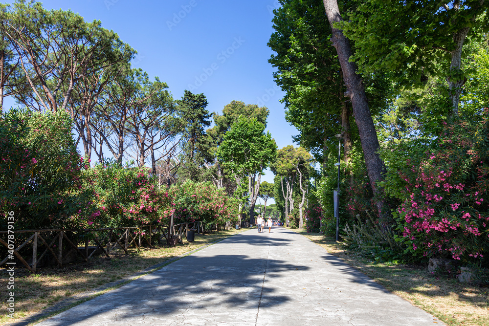 Pompeii, Company, Italy - June 25, 2019: A street surrounded by lush green trees and flowering shrubs under a generous Italian blue sky in the vicinity of the ancient complex of Pompeii.