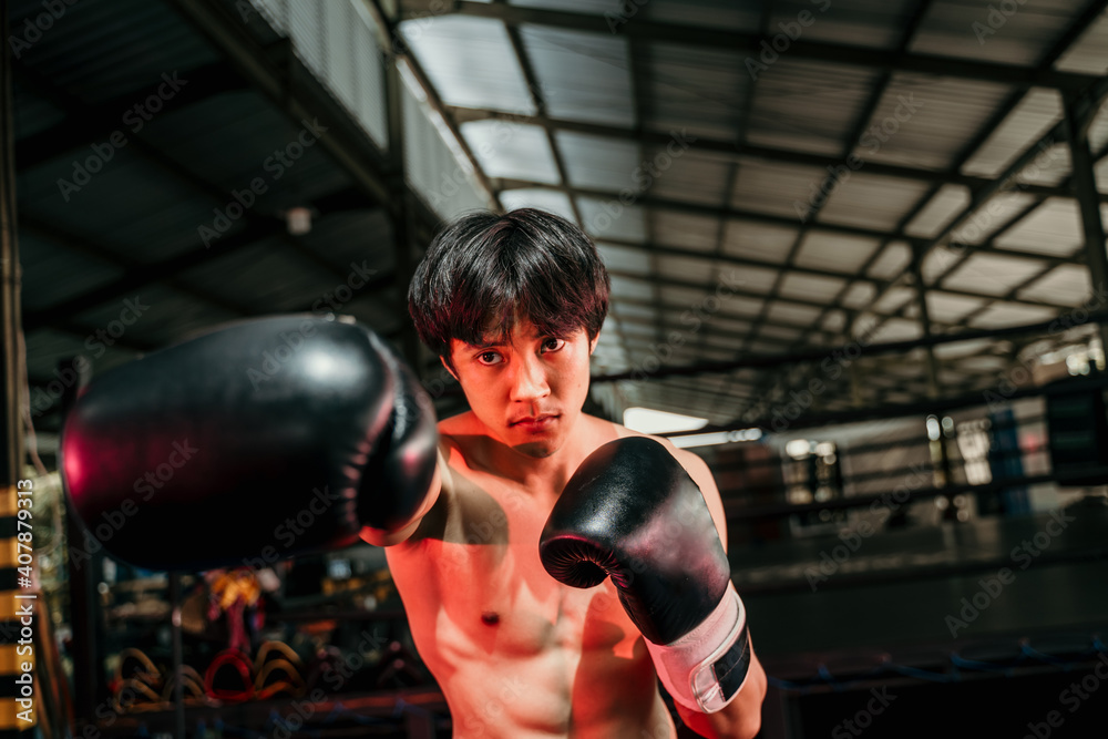 Strong and muscular young man in boxing gear make a hitting motion with the copyspace beside it at boxing training ground background