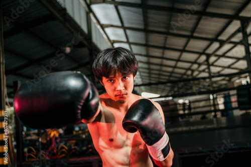 Strong and muscular young man in boxing gear make a hitting motion with the copyspace beside it at boxing training ground background © Odua Images