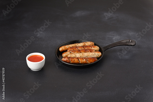 Fried sausages in a frying pan with hot chilisous sauce.