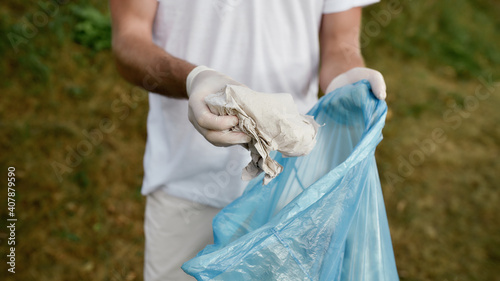 Young male volunteer wearing uniform and rubber gloves collecting trash and garbage in the forest or park, cropped shot