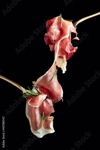 Sliced prosciutto with rosemary on forks.