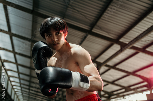 Sportsman muay thai boxer fighting in gloves in boxing cage with the copyspace