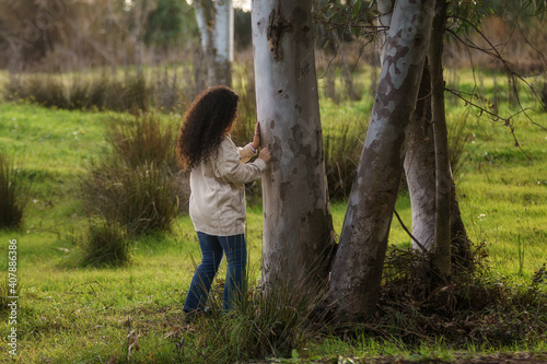 Chica adolescente hispana de pelo negro y rizado grabando un corazón en la corteza de un árbol en invierno.