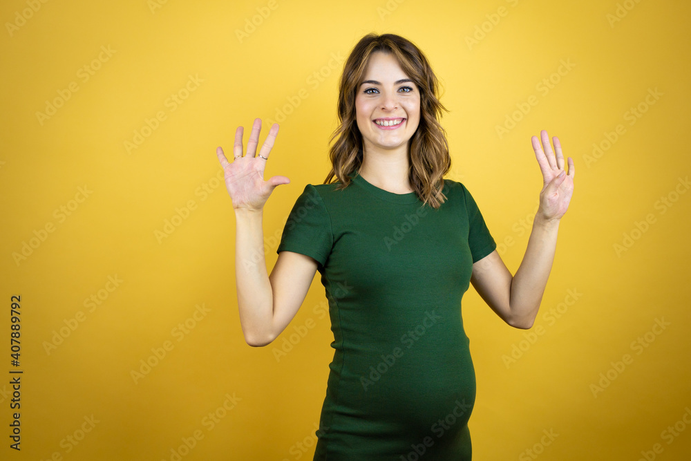 Young beautiful brunette woman pregnant expecting baby over isolated yellow background showing and pointing up with fingers number nine while smiling confident and happy Young beautiful brunette woman pregnant expecting baby over isolated yellow background showing and pointing up with fingers number nine while smiling confident and happy