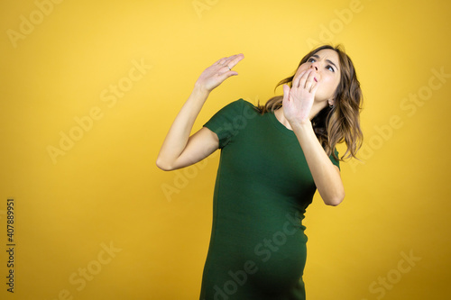 Young beautiful brunette woman pregnant expecting baby over isolated yellow background scared with her arms up like something falling from above photo