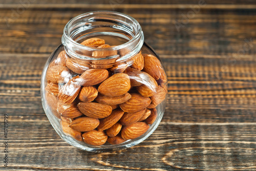 Almonds in a glass transparent jar. Nuts on an old shabby board. Jar on a brown wooden table close up. photo