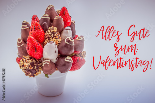 Happy valentine's day greeting card in German that reads Alles Gute zum Valentinstag with red lettering; A bundle of edible flowers, arrangement of strawberries covered in chocolate isolated on white