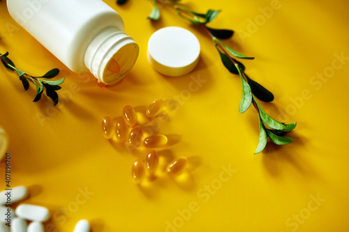 Flat lay of pills, fish oil, vitamins with green leavws on yellow background photo