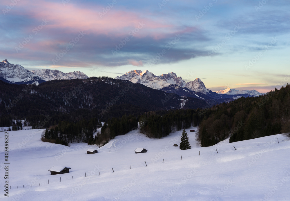 Beautiful sunrise in the mountains with snow covered huts in foreground - Alps with Alpspitze and Zugspitze in background
