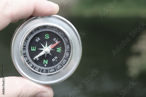 Old classic navigation compass in hand on natural background as symbol of tourism with compass, travel with compass and outdoor activities with compass