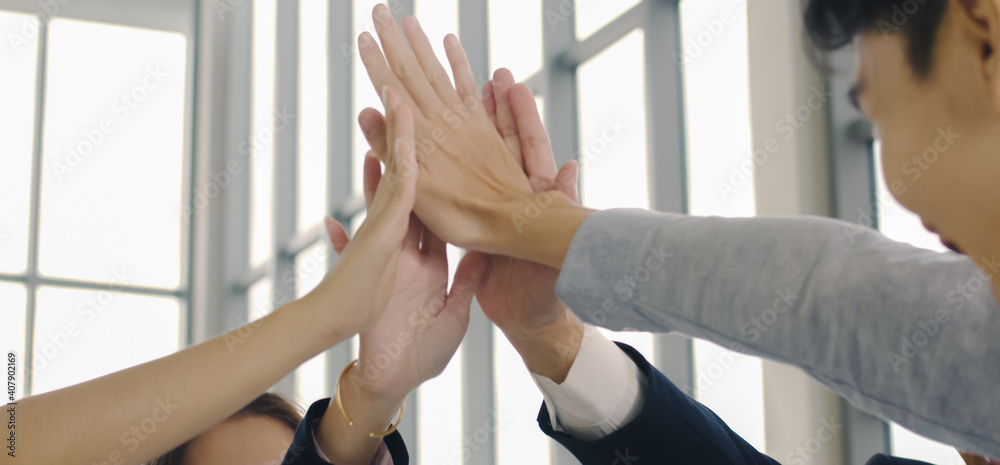 Obraz premium Group of Asian business team people giving hand showing unity and teamwork celebrating success at their working places in the modern office, a business having fun together enjoy achieving goals.