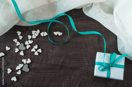 WHITE GIFT BOX WITH TURQUOISE TAPE AND HEARTS ON A WOODEN BACKGROUND. Concept for Valentine's Day.