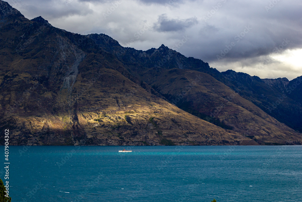 Ship on Lake Wakatipu on a cloudy day next to beautiful sun rays, Queenstown, New Zealand