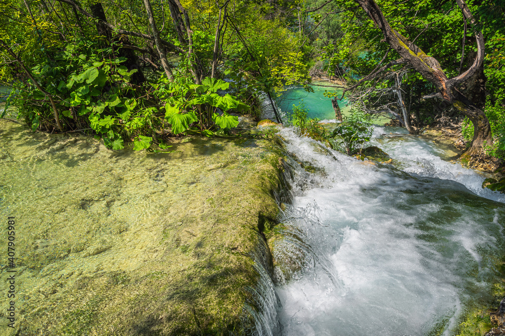 Stream cascading down from rocks, flowing in to turquoise lake surrounded by green forest. Plitvice Lakes National Park UNESCO World Heritage, Croatia Stream cascading down from rocks, flowing in to turquoise lake surrounded by green forest. Plitvice Lakes National Park UNESCO World Heritage, Croatia