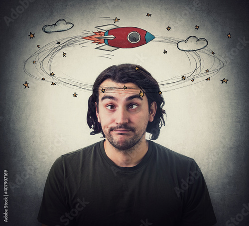 Silly young man makes funny dumb faces with crossed eyes. Body language emotional reaction. Dizzy daydreaming, stars and rocket making circles around his head. Guy suffering from strabismus