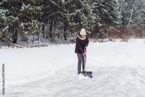 Woman removing snow with a shovel in the winter. Ice rink cleaning