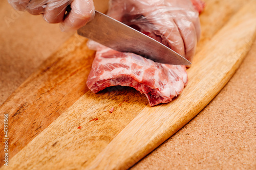 raw pork ribs are cut with a knife on a wooden cutting board. cooking meat at home. hands in disposable gloves. Cook.