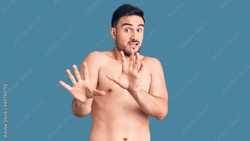 Fototapeta premium Young handsome man wearing swimwear afraid and terrified with fear expression stop gesture with hands, shouting in shock. panic concept.
