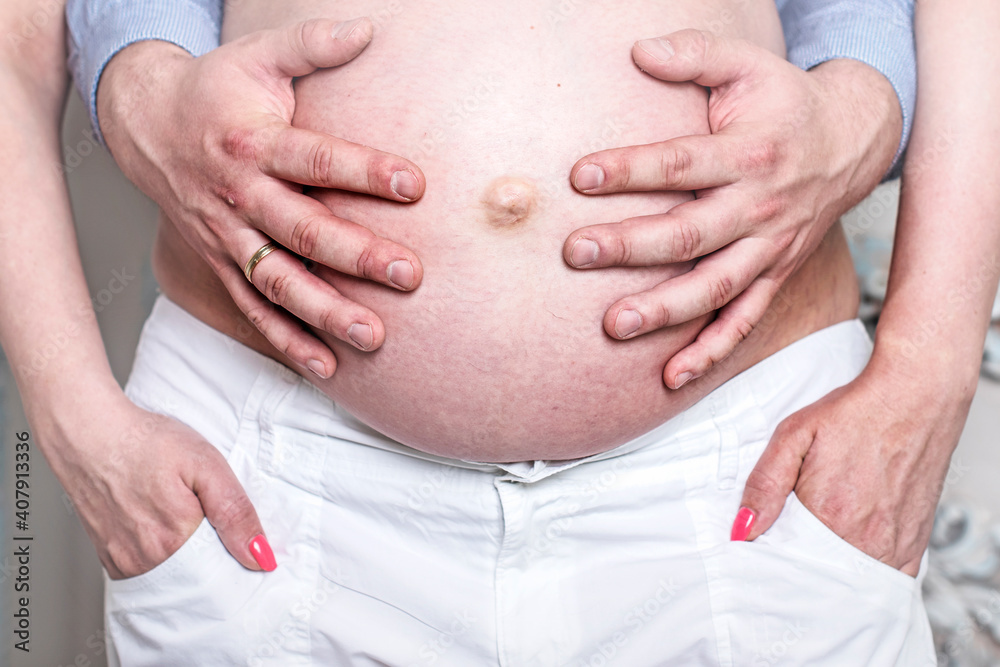 Close-up photo of a naked pregnant tummy. Men's hands hug the belly of their pregnant wife. Close-up photo of a naked pregnant tummy. Men's hands hug the belly of their pregnant wife.