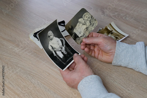 old male hands hold retro family photos over an album with vintage monochrome photographs in sepia color, genealogy concept, ancestral memory, family ties, childhood memories