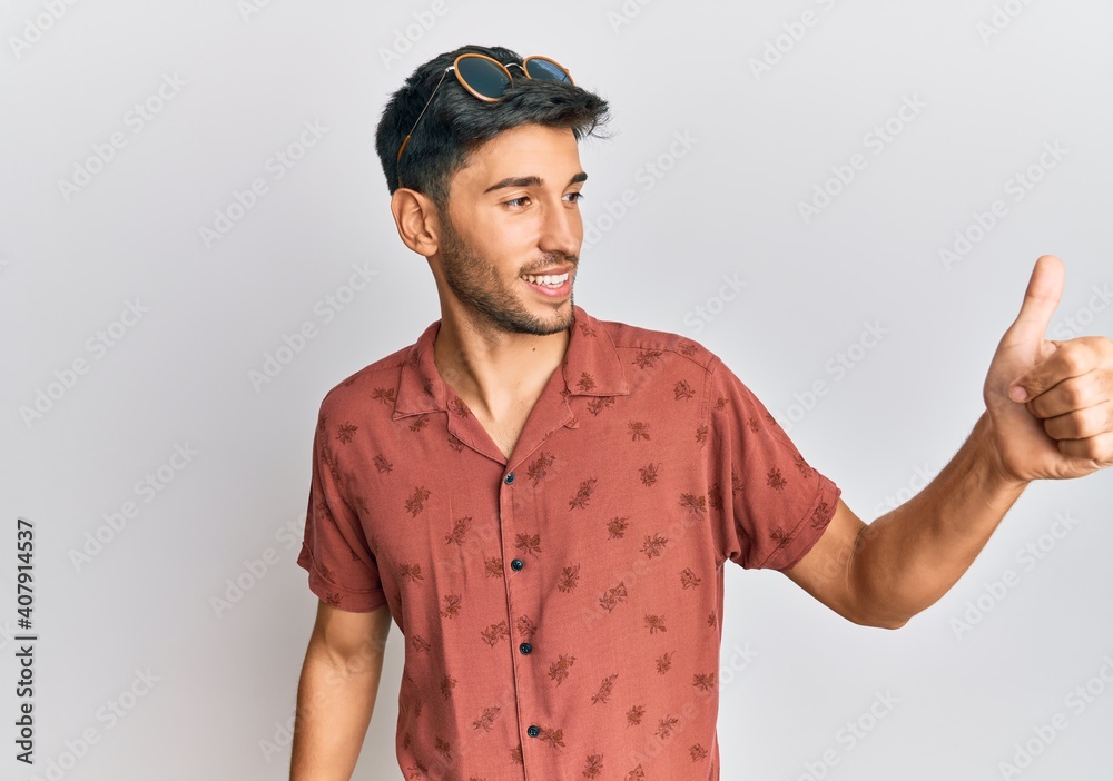 Fototapeta premium Young handsome man wearing casual summer clothes looking proud, smiling doing thumbs up gesture to the side