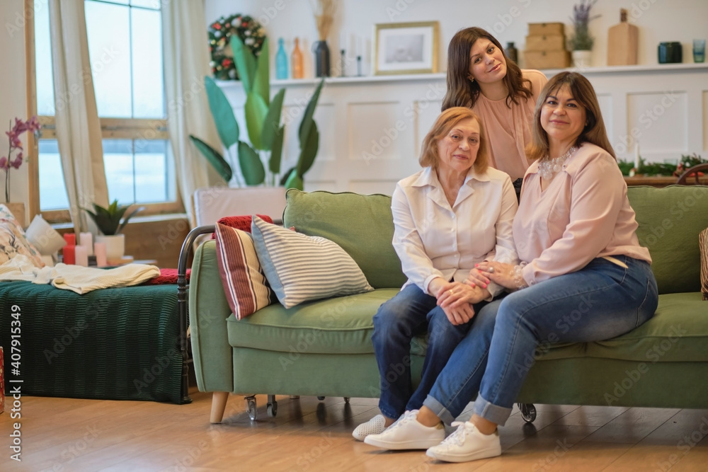 three generations of a family of women are sitting together on the couch. grandmother, daughter, and granddaughter pose together to get a joint photo. three generations of a family of women are sitting together on the couch. grandmother, daughter, and granddaughter pose together to get a joint photo.