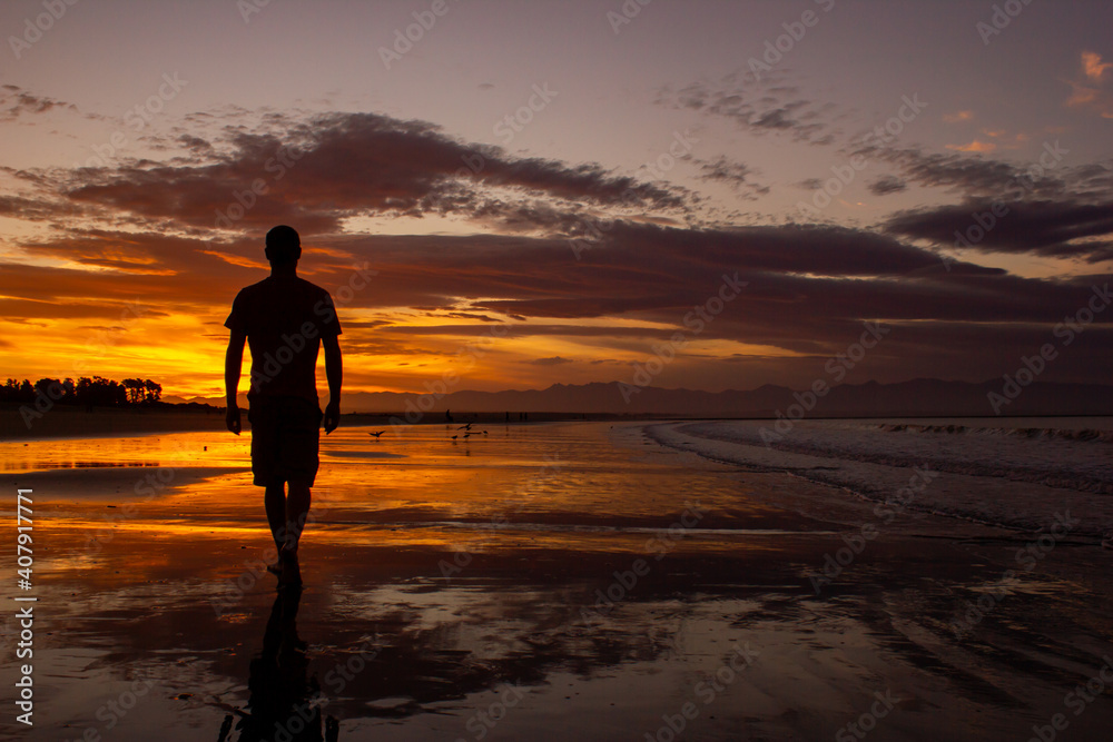 silhouette of a young man walking on the beach in nelson during sunset on Tahunanui Beach at Nelson, New Zealand