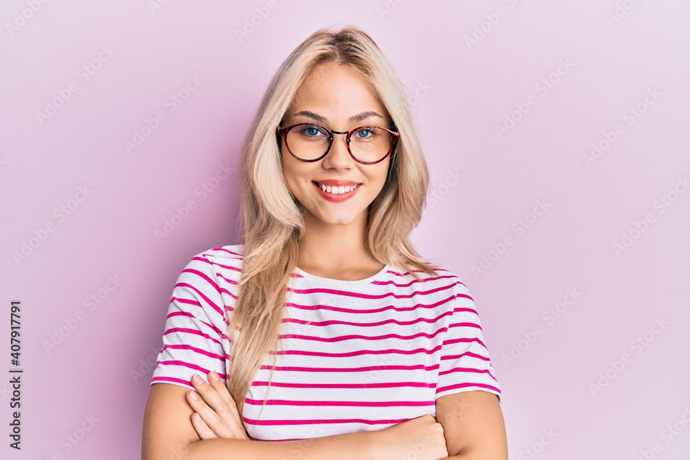 Beautiful caucasian blonde girl wearing casual clothes and glasses happy face smiling with crossed arms looking at the camera. positive person.