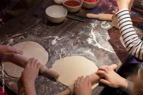 The children's team is learning to make pizza together. A lot of children's hands roll out the dough
