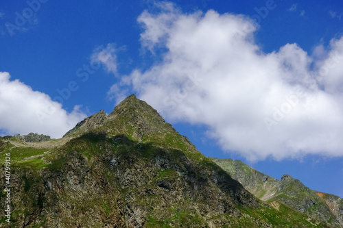 pointed mountain with soft white clouds on the blue sky