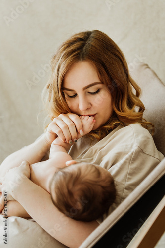 Young mother breastfeeds her newborn on a cloth background in the studio.