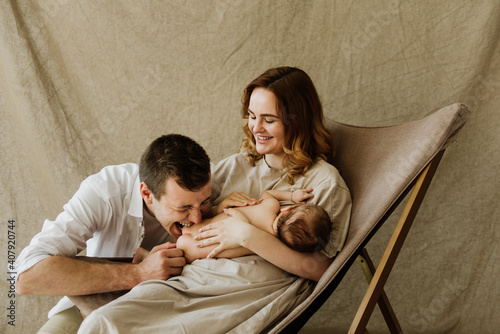 mother and dad is breastfeedin A young mother is breastfeeding a newborn and a young dad is nearby. Young mom and dad are holding a newborn daughter in their arms on a fabric background in the studio.