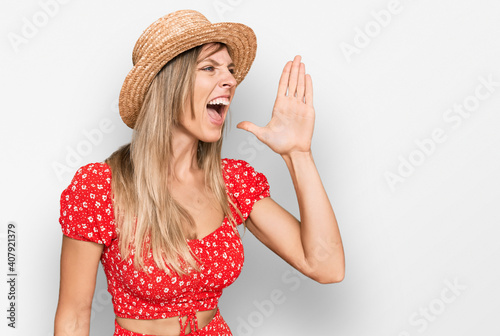 Beautiful caucasian woman wearing summer hat shouting and screaming loud to side with hand on mouth. communication concept.