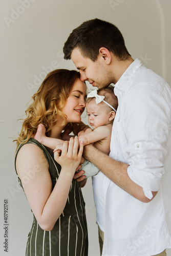 Young parents hug and kiss their newborn daughter on a white background in the studio.