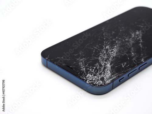 Photo of blue smartphone with broken damaged display. Modern smartphone with damaged glass screen on white background. Device needs repair.