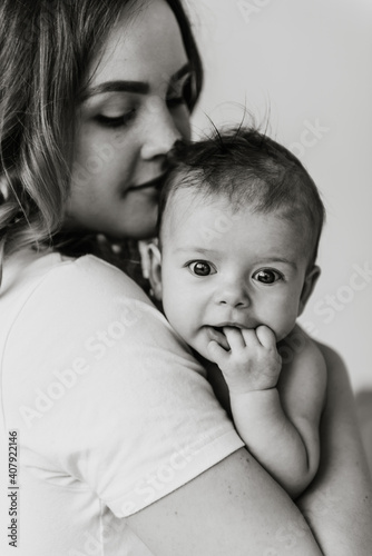 Beautiful mom hugs and kisses the newborn in the studio on a white background. A young mother in a white bodysuit hugs and kisses her newborn daughter in the studio.