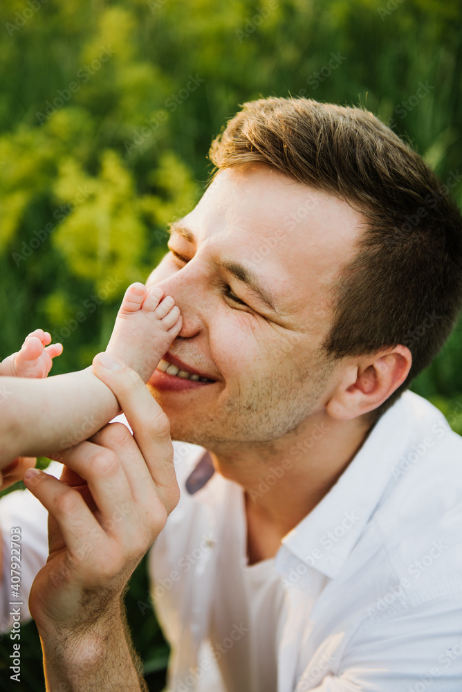 Naklejka premium Young dad kisses the feet of a newborn close-up.